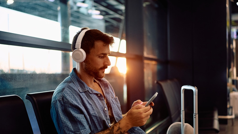 Man with tattoos and headphones on, waiting in an airport.