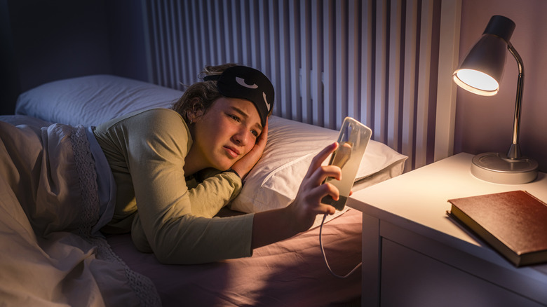 a girl checking her phone while plugged in next to her bed