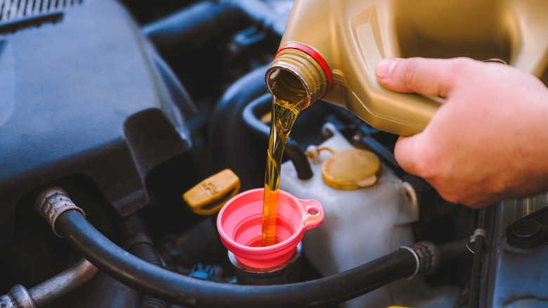Oil being poured into a vehicle's engine via a funnel.