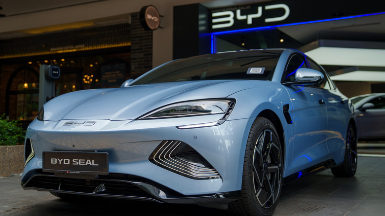 A blue BYD Seal electric sedan parked outside a BYD showroom.