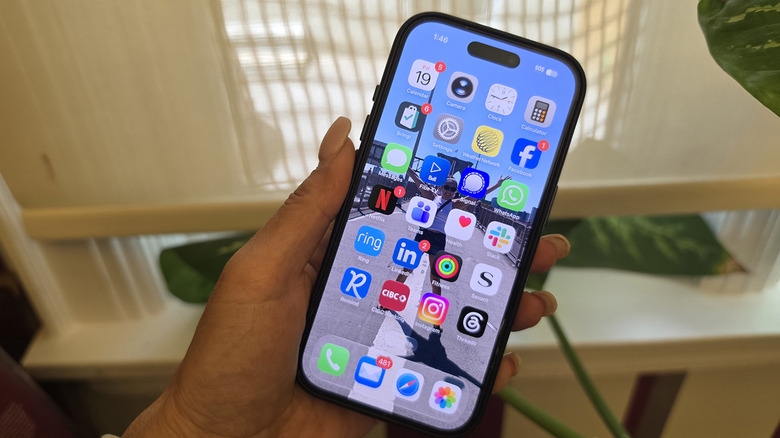 An iPhone in hand by a window with the SOS symbol at the top