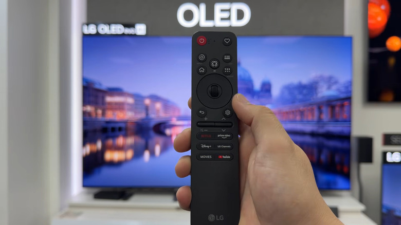 Hand holding LG TV remote 2026 in front of LG TV OLED