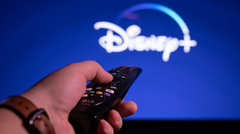Hand holding LG TV remote and pointing at Disney+ on the TV