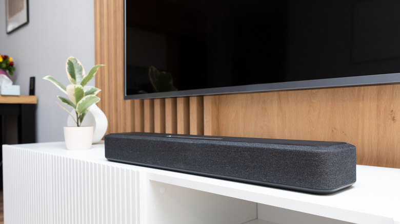 A soundbar on a cabinet next to a plant, under a TV