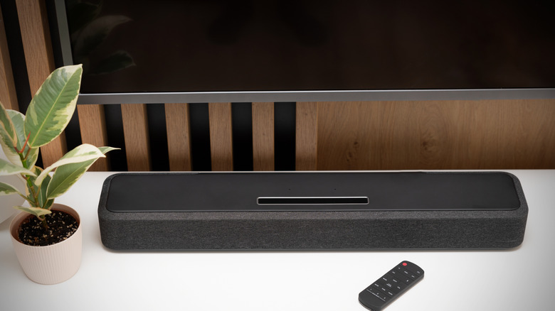 A soundbar on a cabinet next to a plant, under a TV