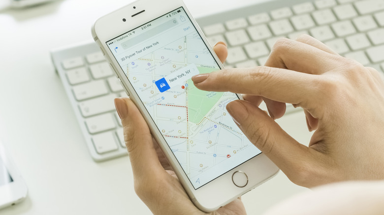 A person using the Apple Maps app on an iPhone, in front of a desktop keyboard.