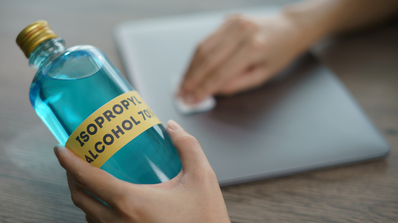 a person holding isopropyl alcohol bottle while cleaning a laptop in the background