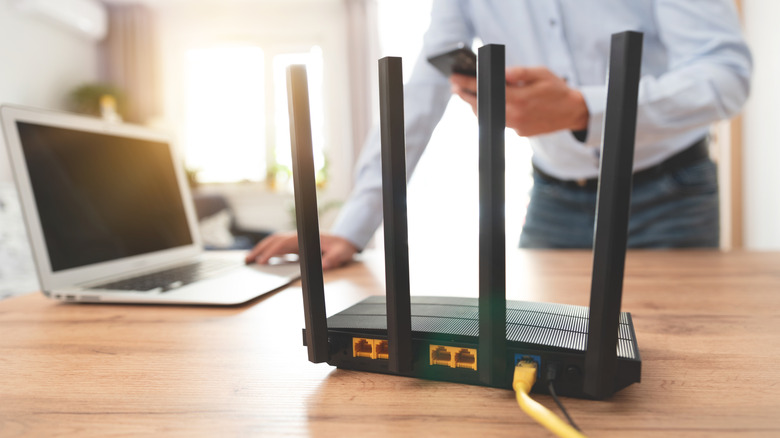 Router in foreground connected via Ethernet with laptop in background.