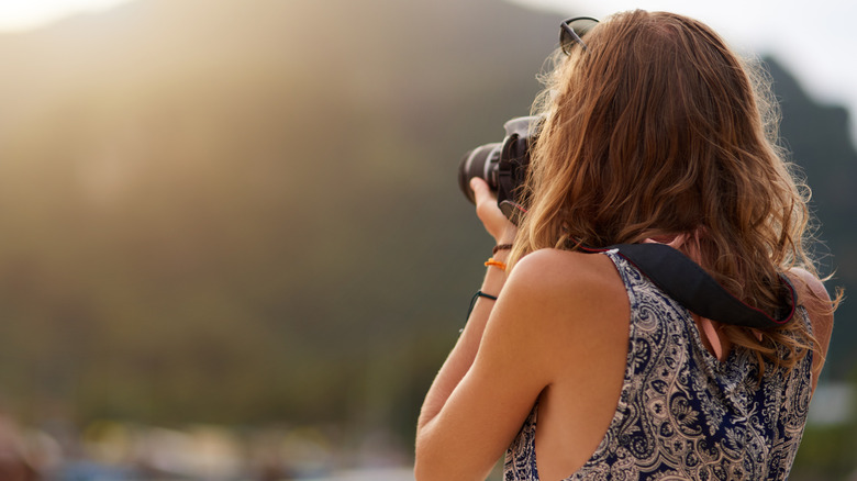 Woman using a DSLR camera to capture photos of a landscape.