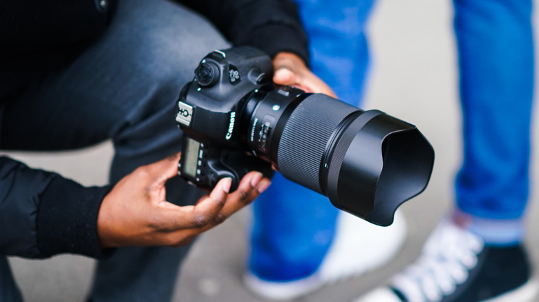 Someone holding a Canon DSLR camera with a powerful lens.
