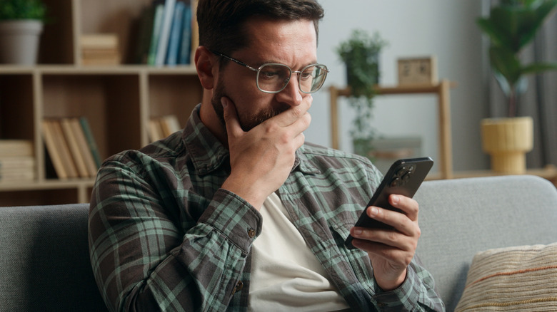 Caucasian adult man male guy at home living room nervous looking at mobile phone