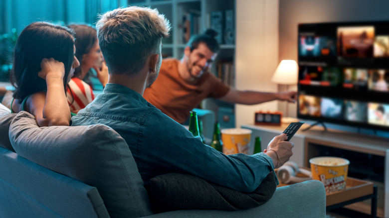 Four friends in a living room with popcorn getting ready to watch a movie