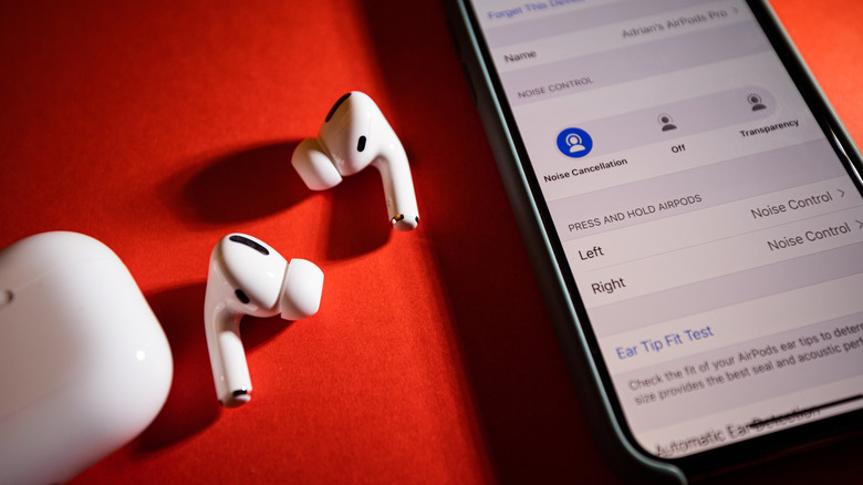 The AirPods Pro placed next to their charging case and an iPhone displaying AirPods Pro customizations.