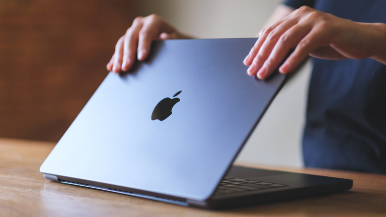 Close-up of a person closing the lid of a MacBook Pro laptop placed on a wooden table
