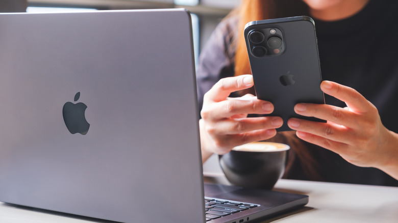 Close-up of a person using an iPhone with a MacBook and a coffee mug in the frame
