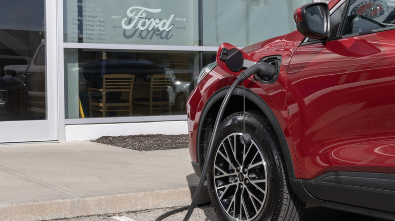 A Ford Escape Base Hybrid SUV being charged in front of a Ford building.