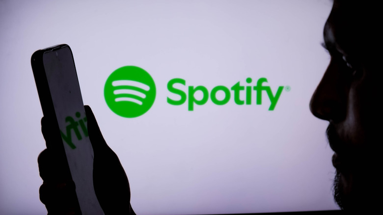 a person holding a mobile device next to the Spotify logo on a white screen