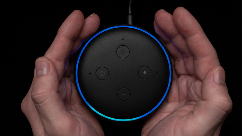 An Echo Dot device in someone's hands displaying a cyan on blue light