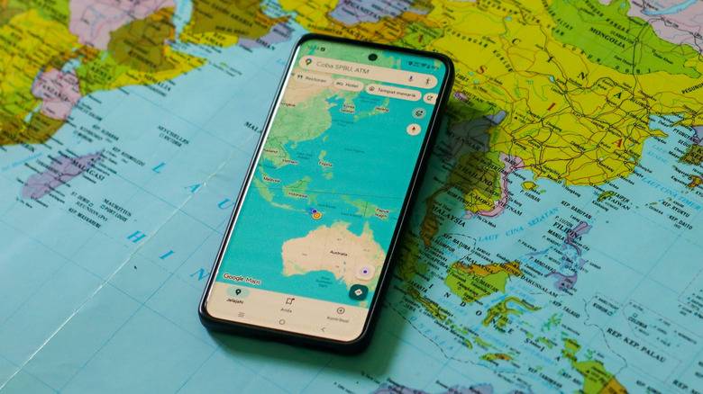 Google Maps loaded on a smartphone that's placed atop of a paper world map.