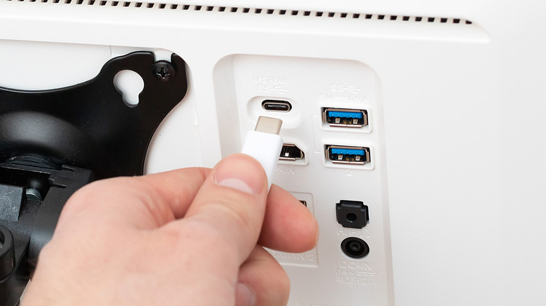 Someone plugging a USB Type-C cable into the back of a display.