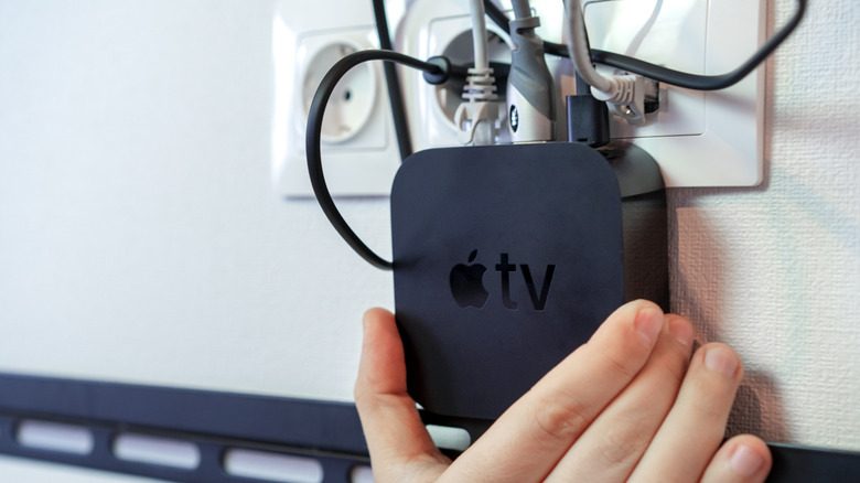 A close up of a hand plugging a black Apple TV device into the wall