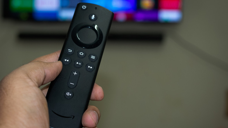 A person pointing an Amazon Fire TV Stick remote toward a TV.