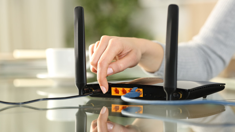 Woman pressing the reset button on the back of a wireless router.
