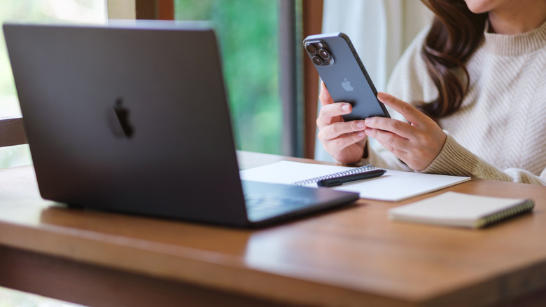 A person sitting and using an iPhone and a MacBook