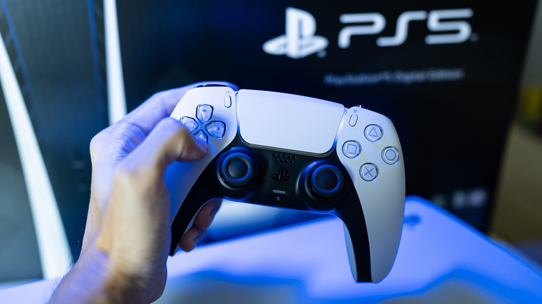 A person holding a PS5 DualSense controller in front of a PS5 box.