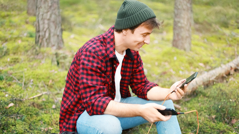 a man sitting outside with two charged phones sitting on a log
