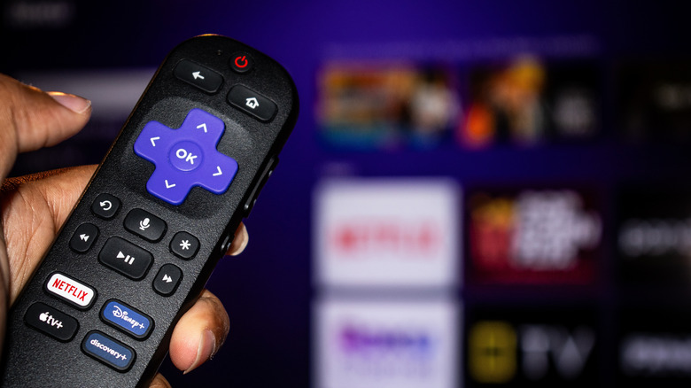 Close up of a hand using a Roku remote to control a TV