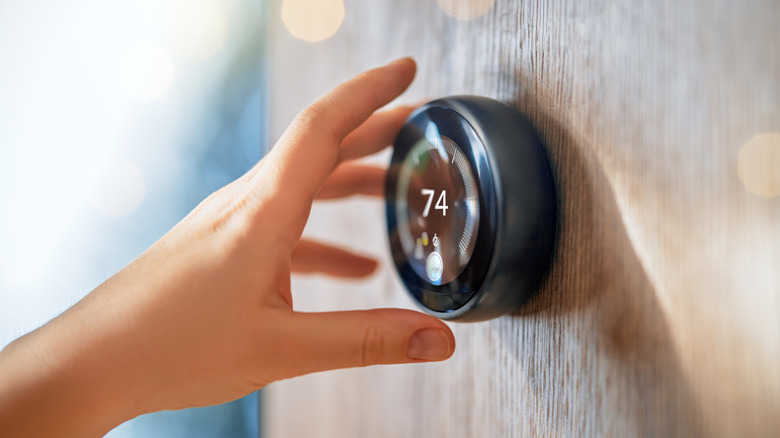 Homeowner adjusting their smart Nest thermostat with their hand.