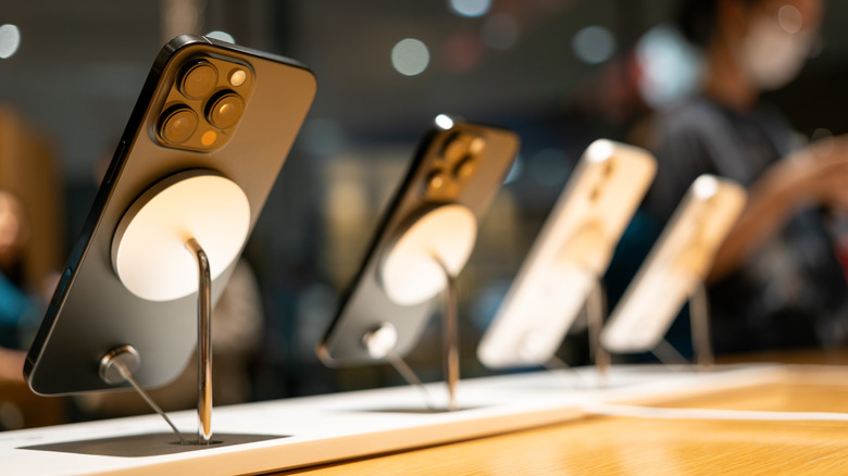 A row of iPhone devices, photographed from behind, displayed at a retail outlet.