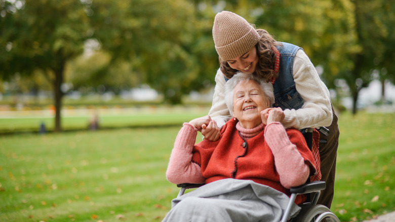 An old woman in a wheelchair being hugged by a younger woman who's standing behind her