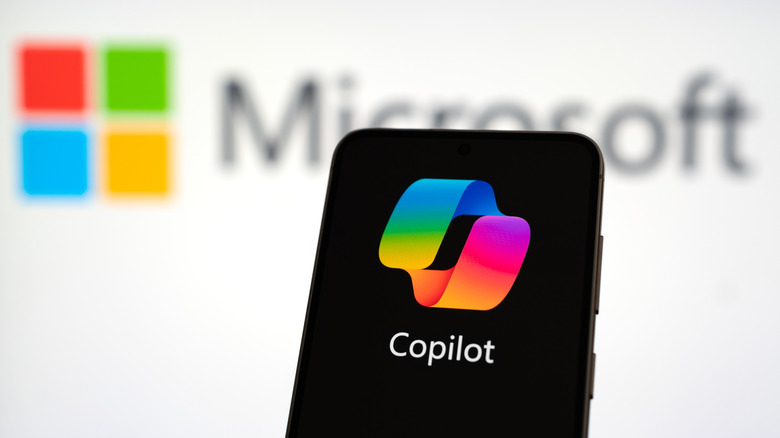 A phone displaying the Microsoft Copilot logo in front of the Microsoft logo