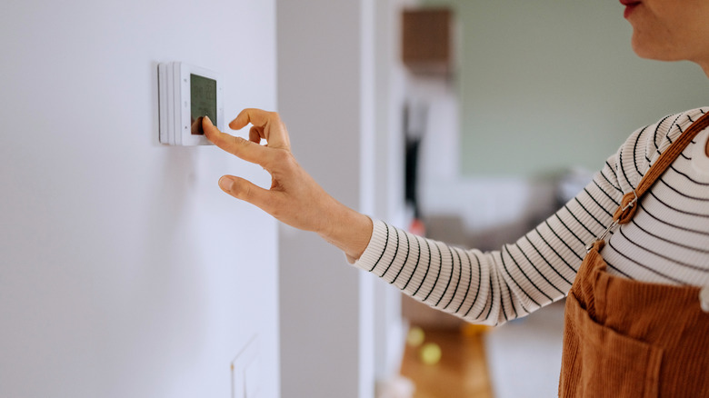 Woman interacting with a digital thermostat on the wall.