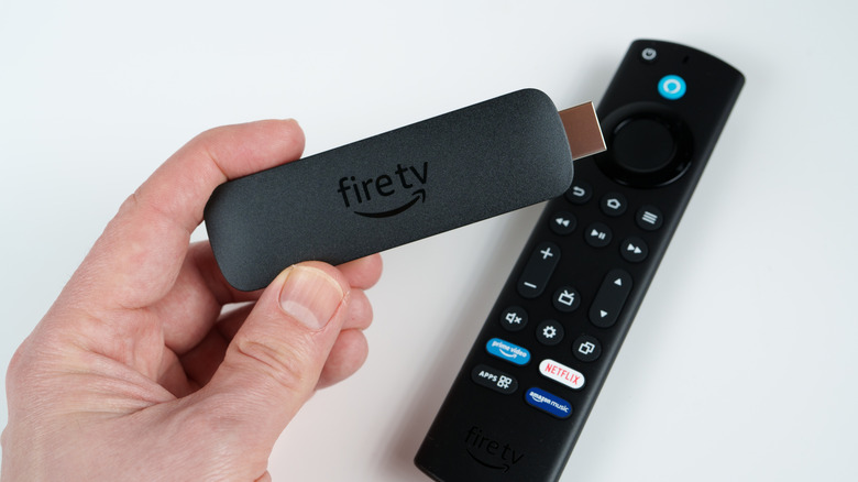 A person holding an Amazon Fire TV Stick in front of its remote.