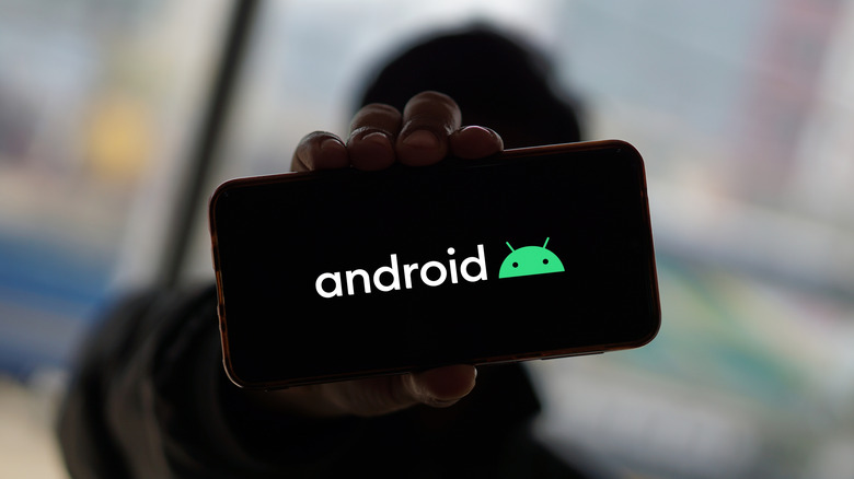 A person holding up a smartphone with the Android logo.