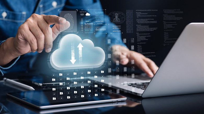 A person on a laptop with an image of a cloud and files hovering in front.