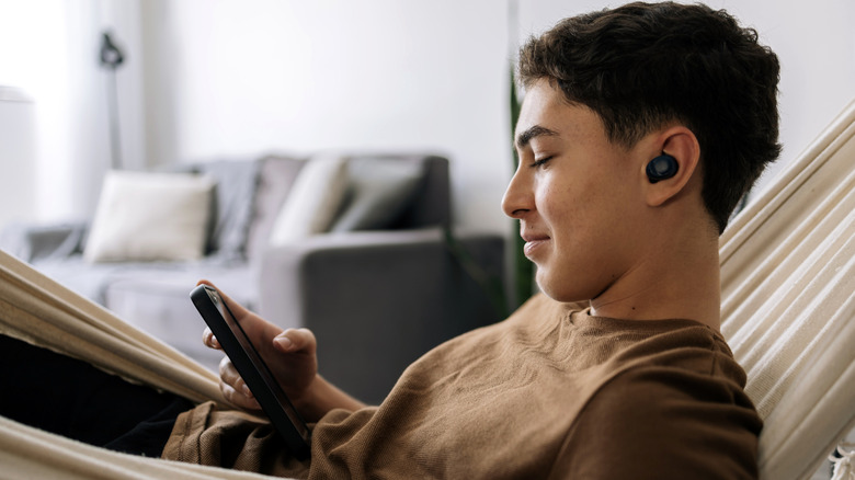 A person using a smartphone while using earbuds for audio