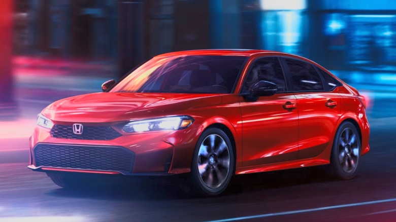 Red Honda Civic sedan hybrid driving through a city street at night