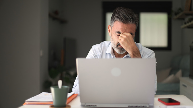 A man sitting on front of a laptop, rubbing his eyes
