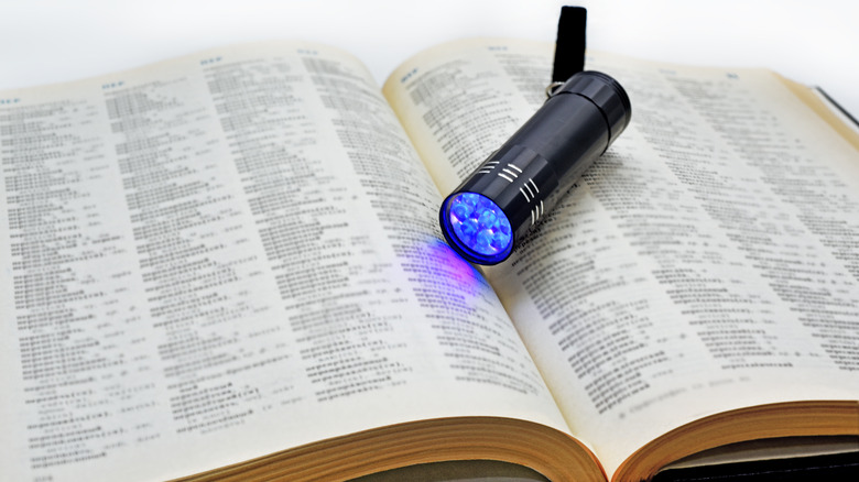 An old book open with a UV black light flashlight turned on and resting on top.