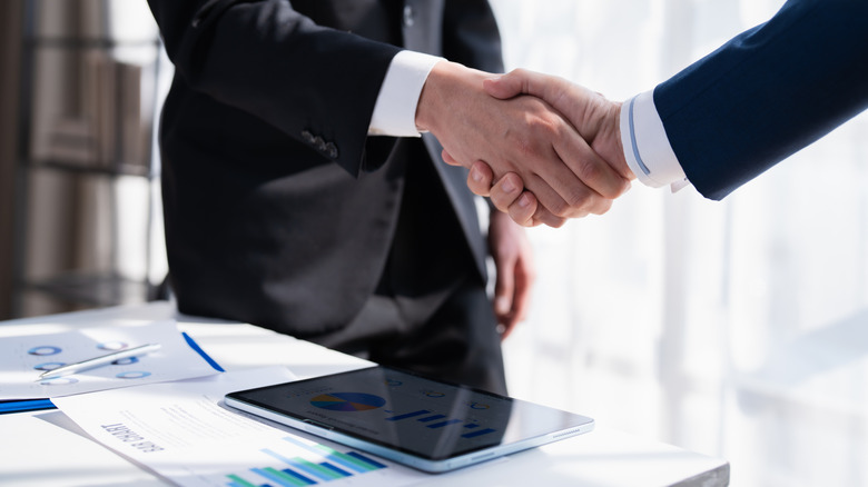 a professional handshake done over a tablet that is sitting on a table