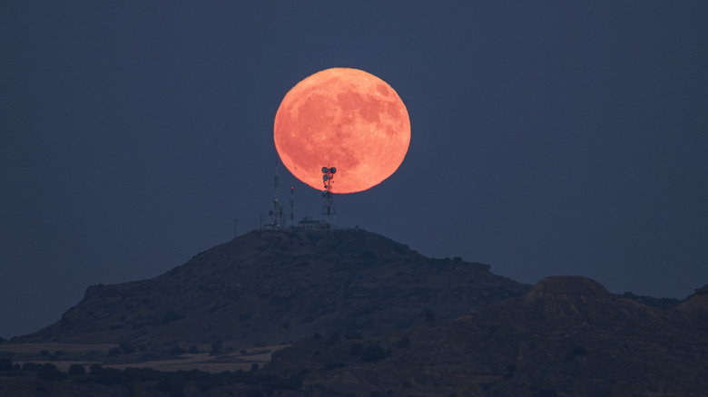 A supermoon rising above the mountains with a telecommunications tower visible.