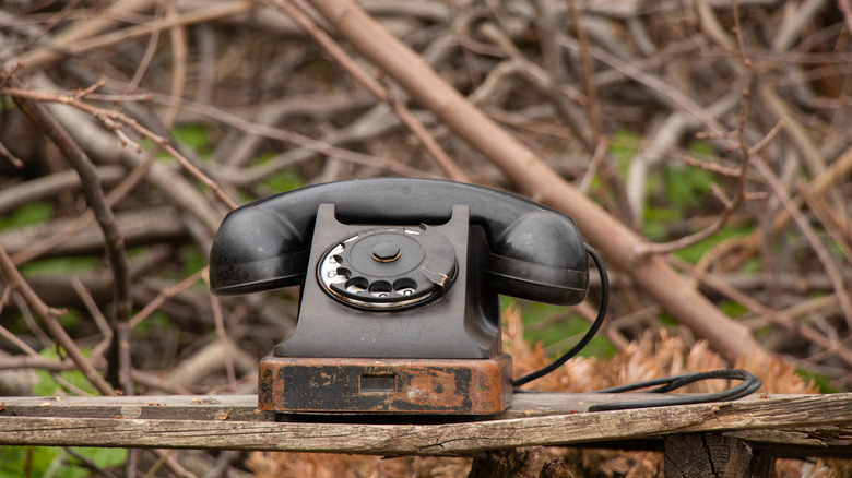 An old rotary dial phone resting atop a table outdoors.