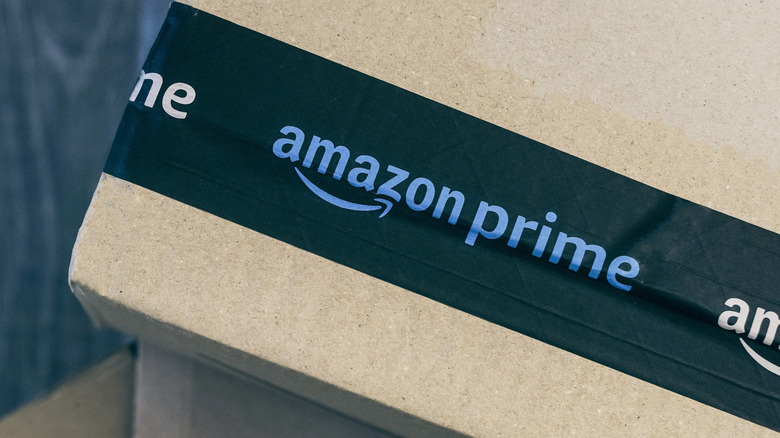 A stack of cardboard packages sit on top of one another, whereas the photo focuses exclusively on the Amazon Prime logo adorning the black packaging tape of one of the boxes