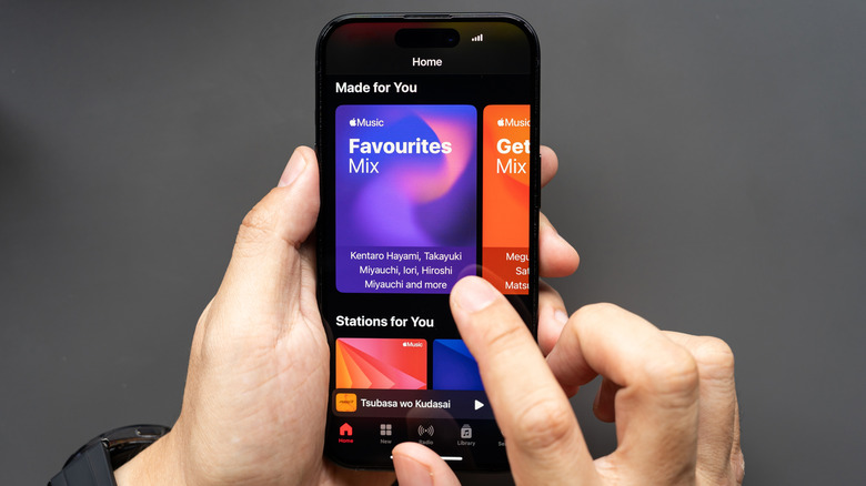 Hands holding an iPhone with a finger tapping on the screen that is showing Apple Music.