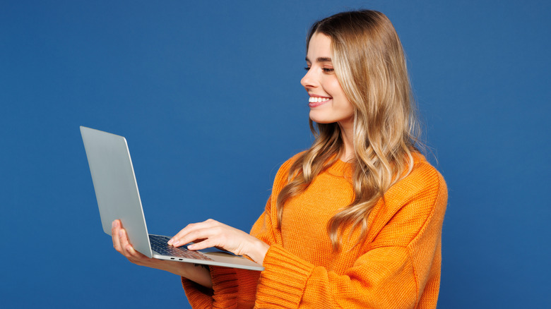 A woman standing up while holding a laptop in their hand over a blue background