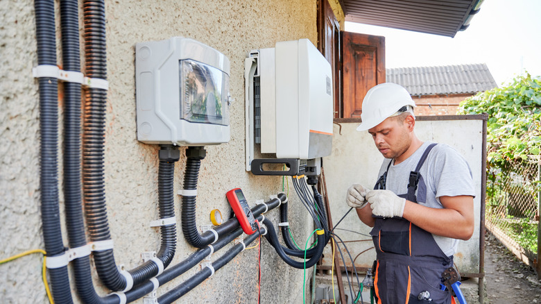 An electrician installing a solar-powered system on the side of a house.